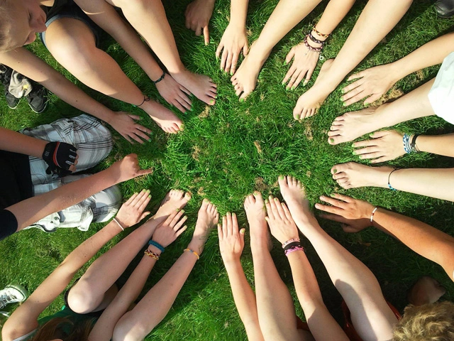 Zdjęcie ludzi, którzy dotykając dłońmi trawy, tworzą krąg na znak wspólnoty